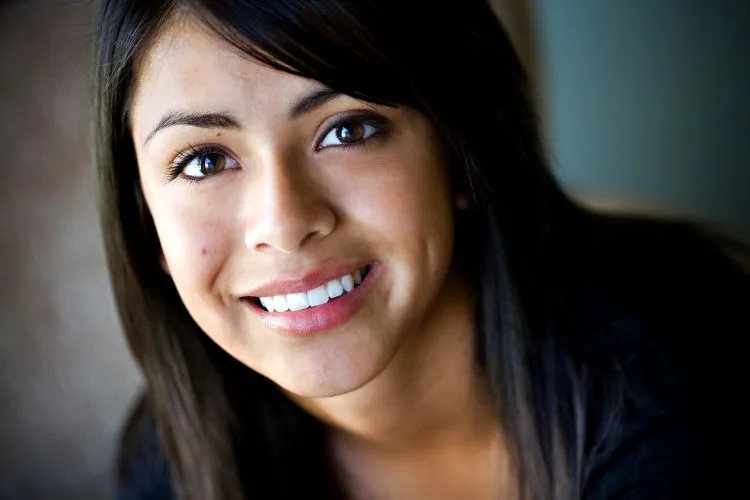 Close-up of a young woman with long dark hair and a bright, symmetrical smile.