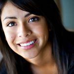 Close-up of a young woman with long dark hair and a bright, symmetrical smile.