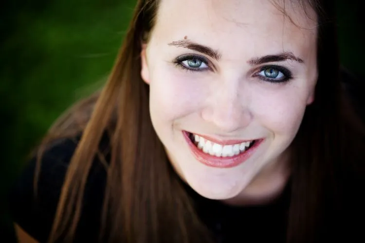 A woman with long dark hair and blue eyes, showing a wide, toothy grin.