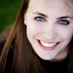 A woman with long dark hair and blue eyes, showing a wide, toothy grin.