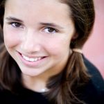 Portrait of a young girl with brown hair in pigtails, smiling happily.