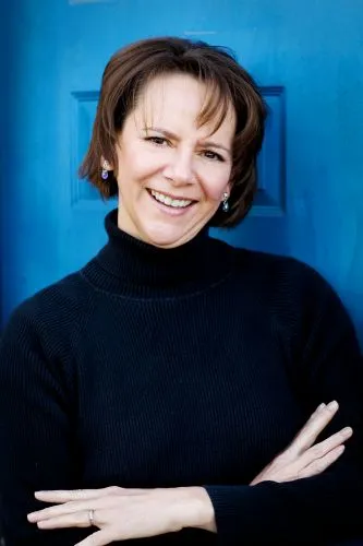 A woman with short, curly dark hair posing against a bright blue background.