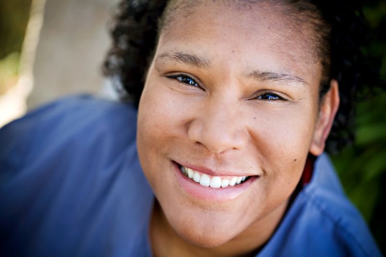 A woman with short, dark curly hair and a warm, friendly expression.