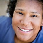 A woman with short, dark curly hair and a warm, friendly expression.