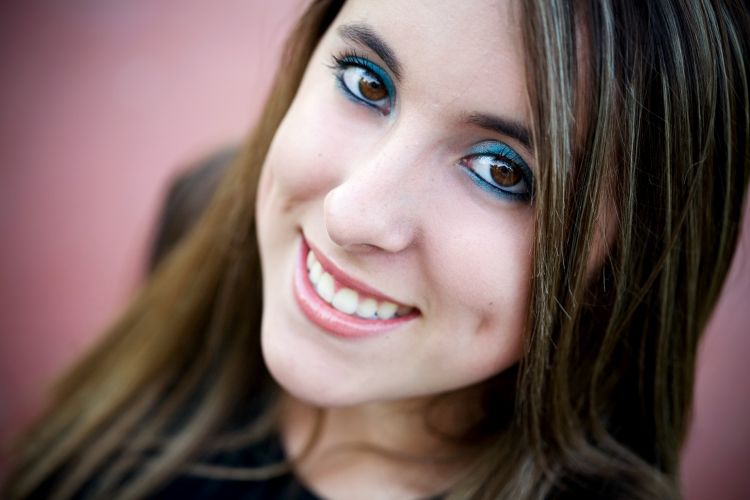 A close-up, slightly tilted headshot of a young woman with long brown hair and a bright smile.