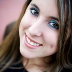A close-up, slightly tilted headshot of a young woman with long brown hair and a bright smile.