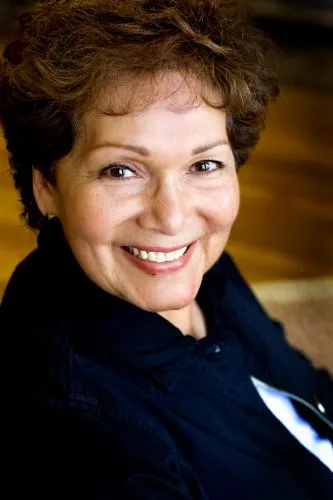 A woman with short, reddish-brown curly hair and a joyful, wide smile.