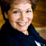 A woman with short, reddish-brown curly hair and a joyful, wide smile.