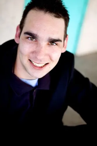 Close-up of a young man with short dark hair, leaning forward with a wide grin.