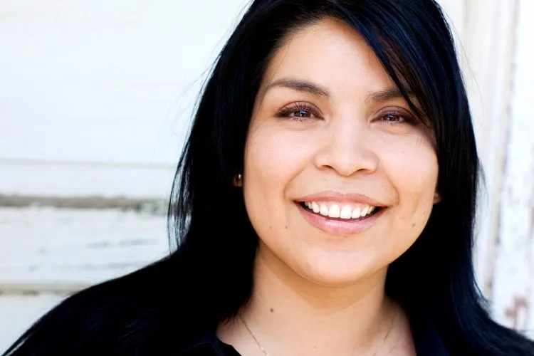 A woman with long, dark straight hair and a wide, beaming smile.