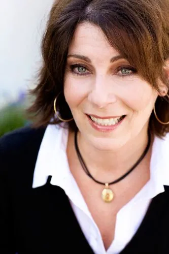 A woman with shoulder-length brown hair and a black necklace, smiling gently.