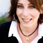 A woman with shoulder-length brown hair and a black necklace, smiling gently.