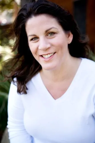 Portrait of a woman with dark wavy hair wearing a white V-neck shirt, smiling warmly.