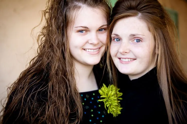 Two young girls with long brown hair posing closely together, both smiling.