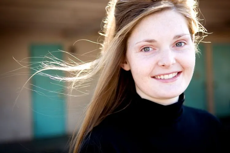 A young woman with blonde hair looking at the camera with a soft, cheerful smile.