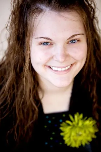 Headshot of a teenage girl with long dark hair and a gentle smile, wearing a dark top.