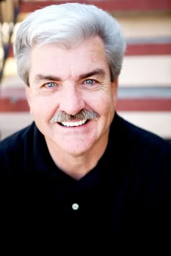 Portrait of an older man with short grey hair, wearing a black shirt and smiling.